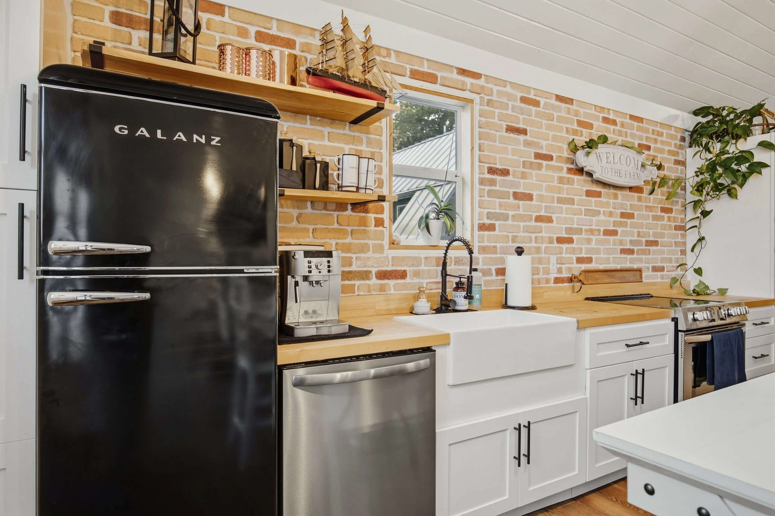 Farmhouse kitchen with black refrigerator, white sink, brick wall and stove
