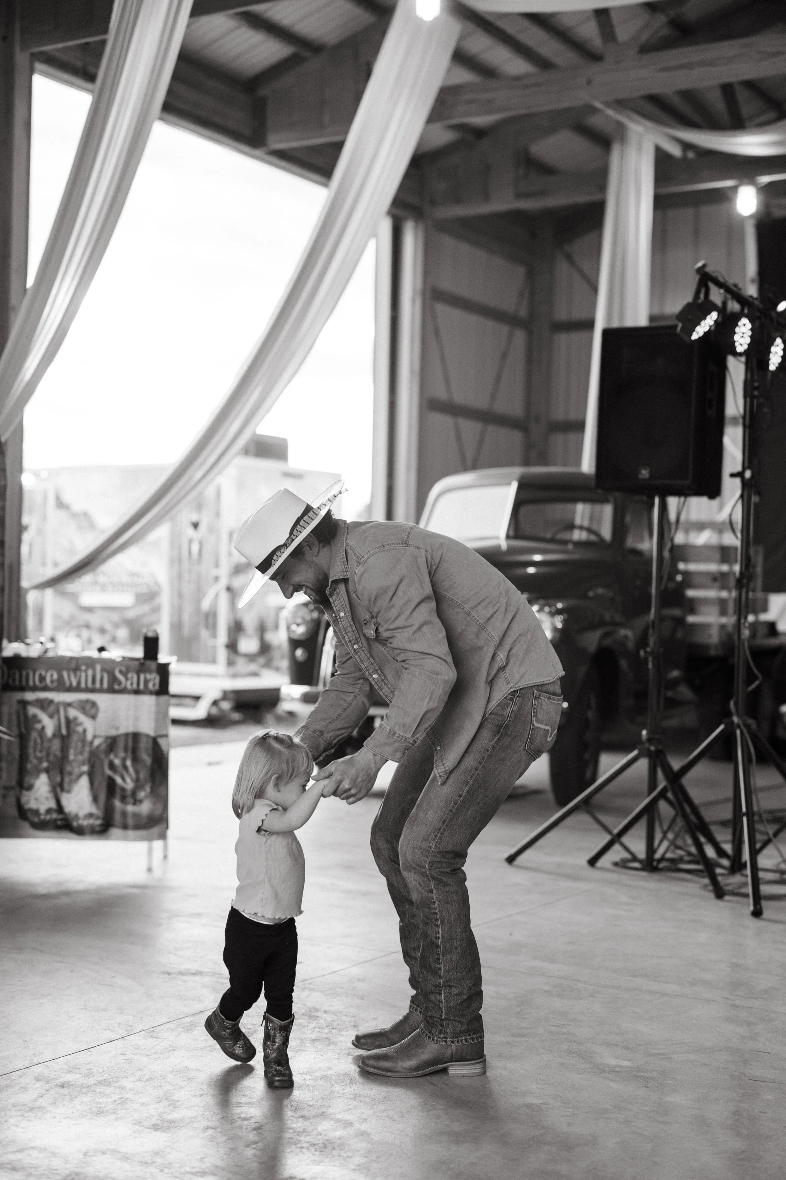A guest dancing with a toddler in the barn in black and white