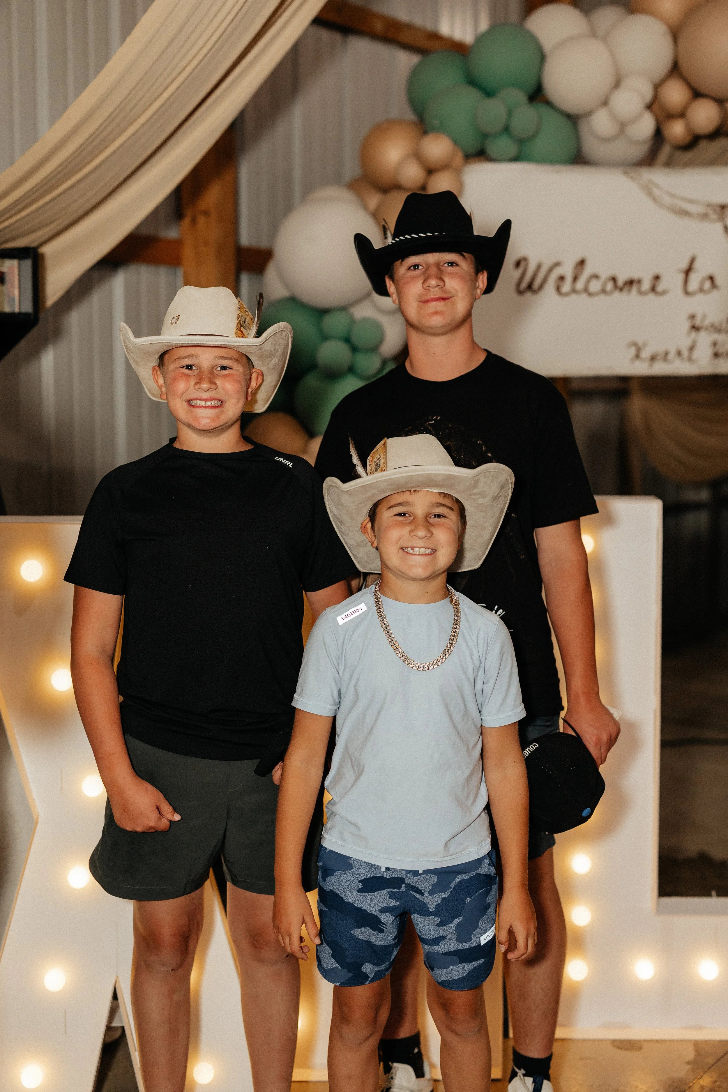 Three young guests in cowboy hats posing beside celebration decorations