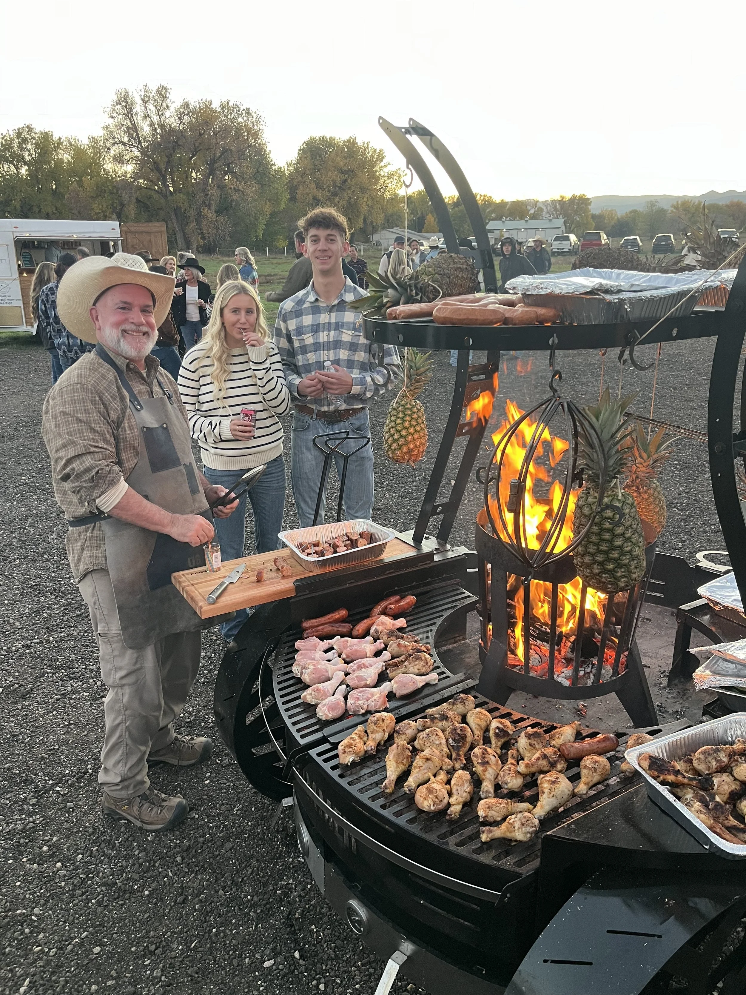 Guests enjoying dinner beside the open-fire grill at a farm gathering