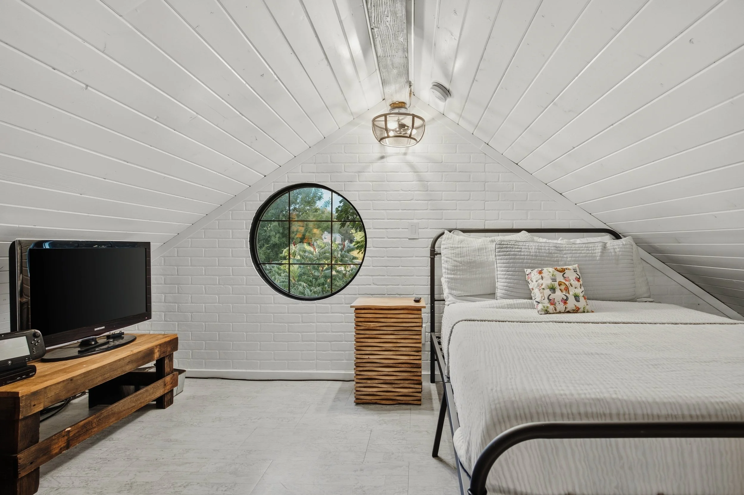 Upper sleeping loft with white bedding, round window and television