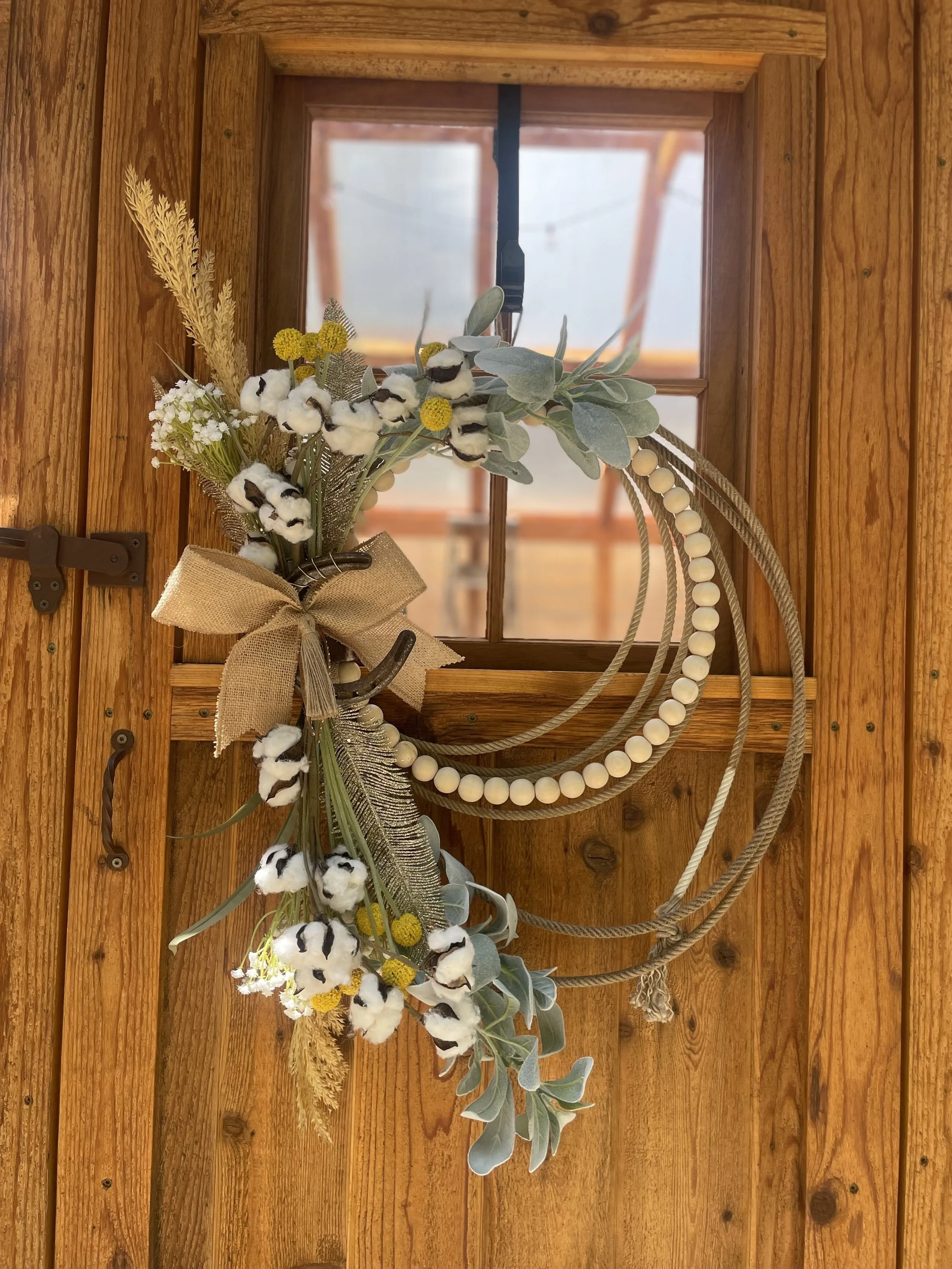 Handcrafted wreath with greenery, cotton, yellow flowers, beads and horseshoes on a wooden door