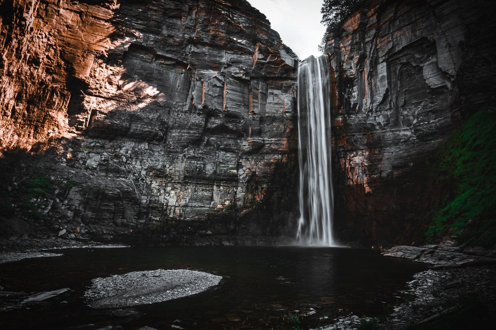 A tall waterfall descends into a dark pool between steep rock walls.