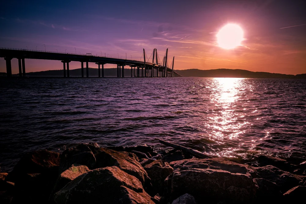 A bridge crosses the water beneath a glowing pink and purple sunset.