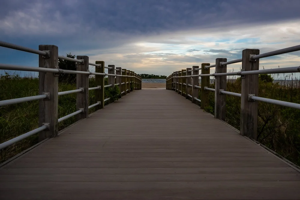 A wooden boardwalk leads toward the horizon beneath a cloudy evening sky.