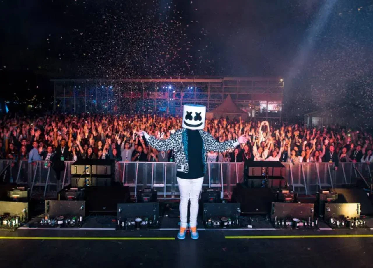 A DJ in a white marshmallow-shaped helmet performs facing the crowd as confetti fills the air at the Forbes Under 30 Summit.