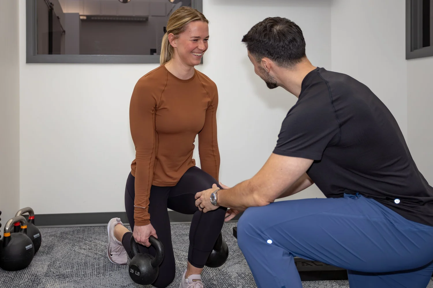 Physiotherapist guiding a patient through a kneeling exercise with a kettlebell