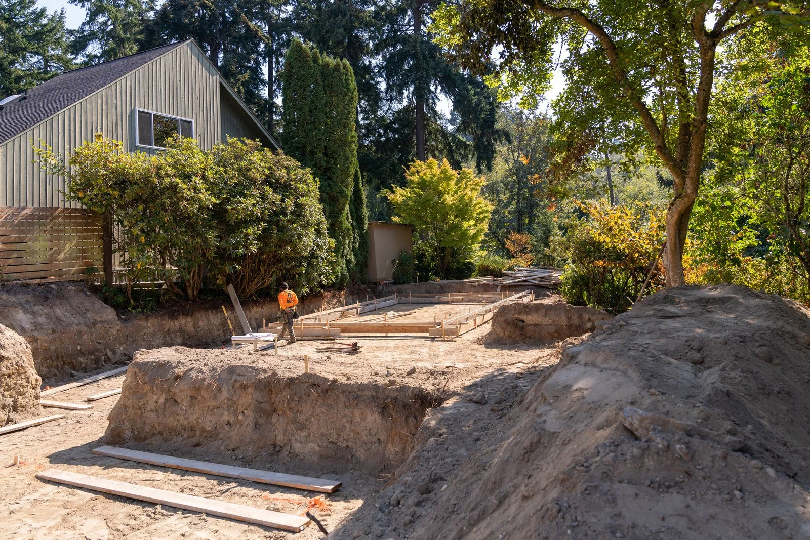 Hillside addition excavation and footing layout behind an occupied home