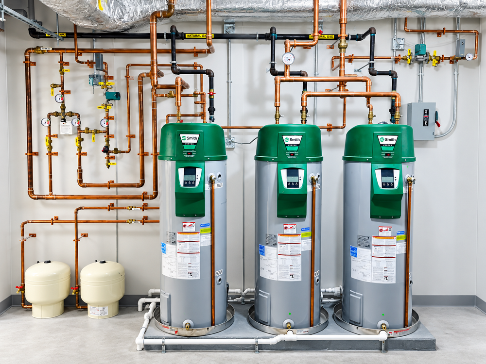 Three green and gray water heaters with copper pipework