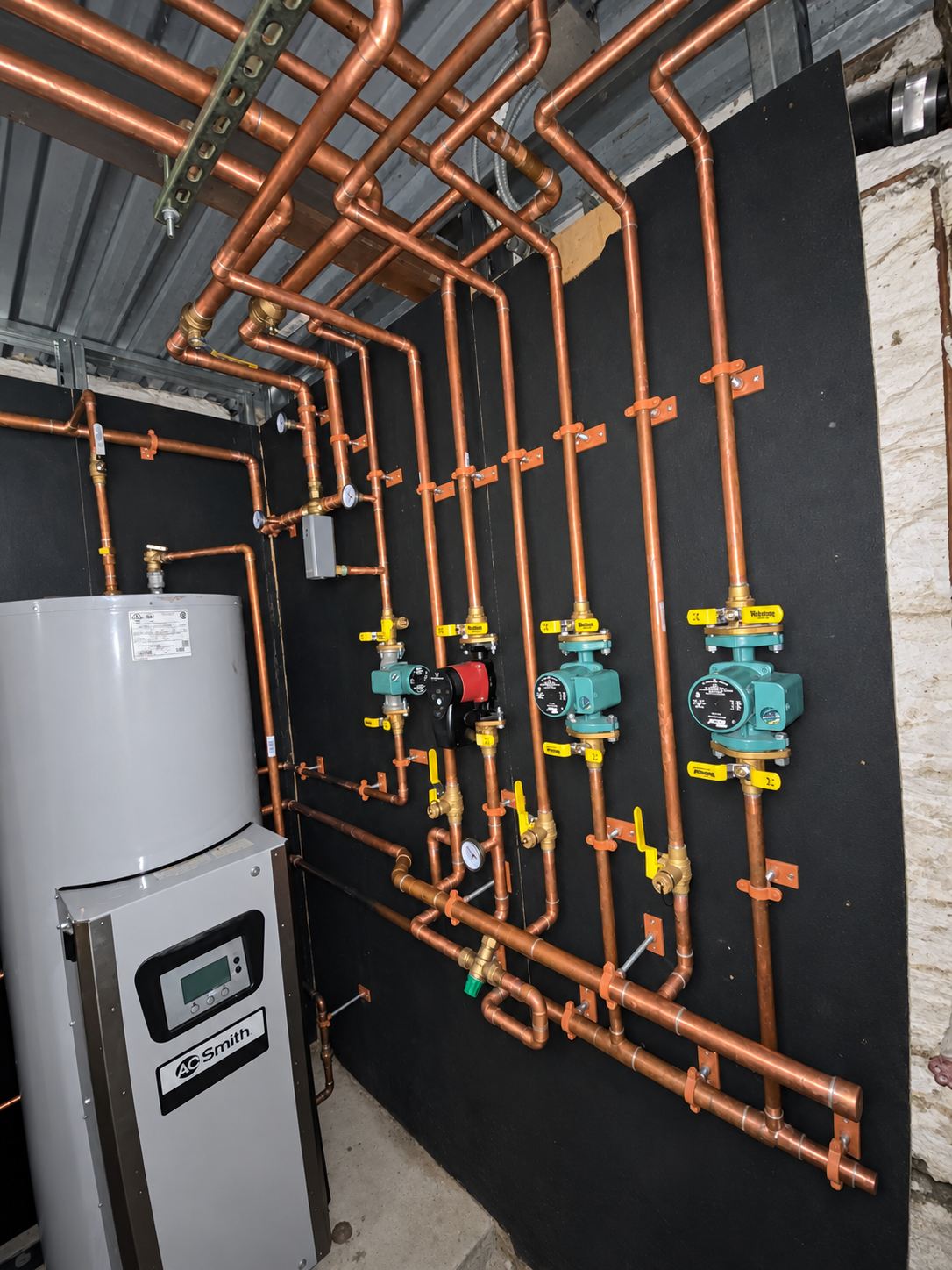 Hydronic heating installation with copper pipework, circulation pumps, valves, and a water heater.