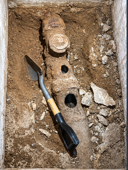 Excavated damaged underground pipe beside a hand shovel