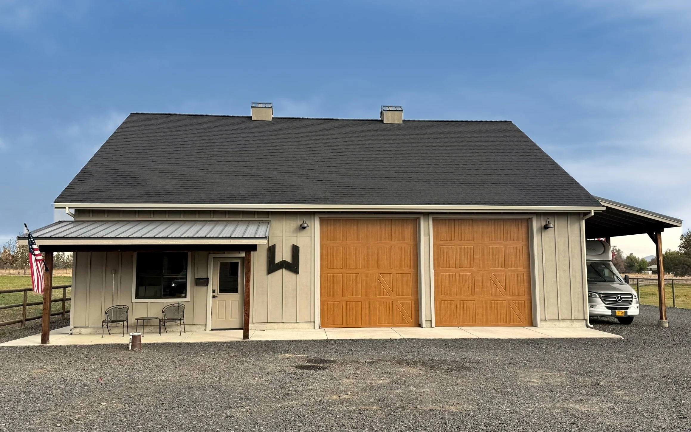 Custom shop built by Wittmer Construction in Central Oregon with board-and-batten siding, two tall wood-tone garage doors, a covered front porch and an attached RV carport