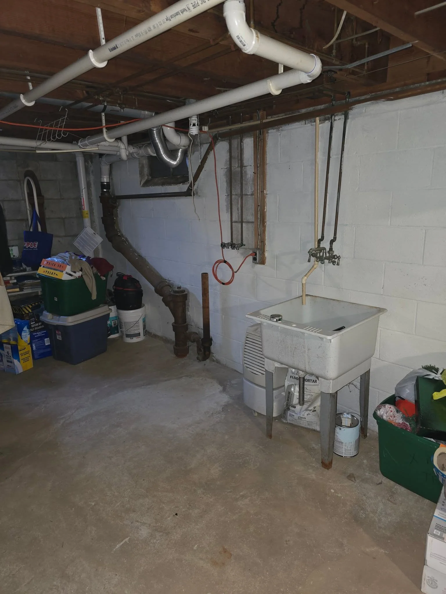 Open basement area before the half bath addition, with a lone wash sink and exposed joists