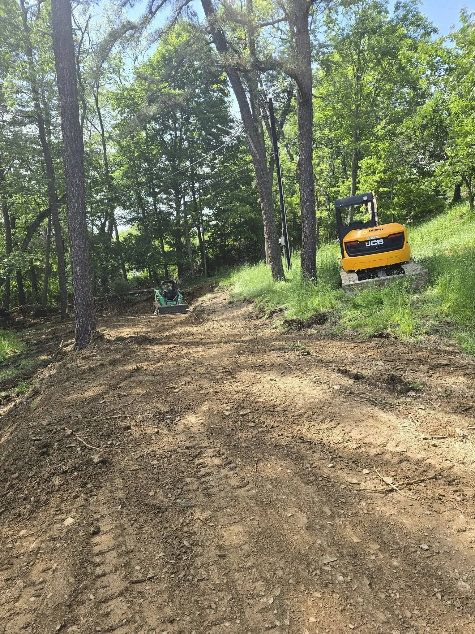 Excavator and grading equipment beside the cleared slope