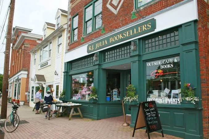 The green storefront of R.J. Julia Booksellers on Boston Post Road in Madison, with sidewalk tables and a chalkboard of upcoming events.