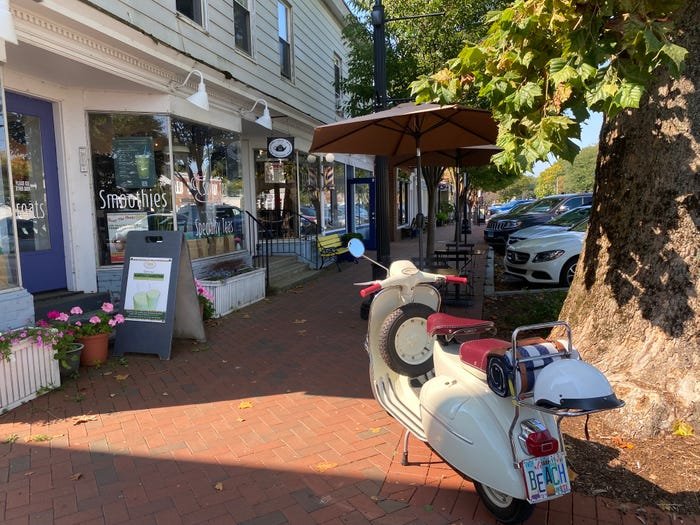 A downtown Madison sidewalk with shopfronts, planters and a vintage scooter parked under a tree.