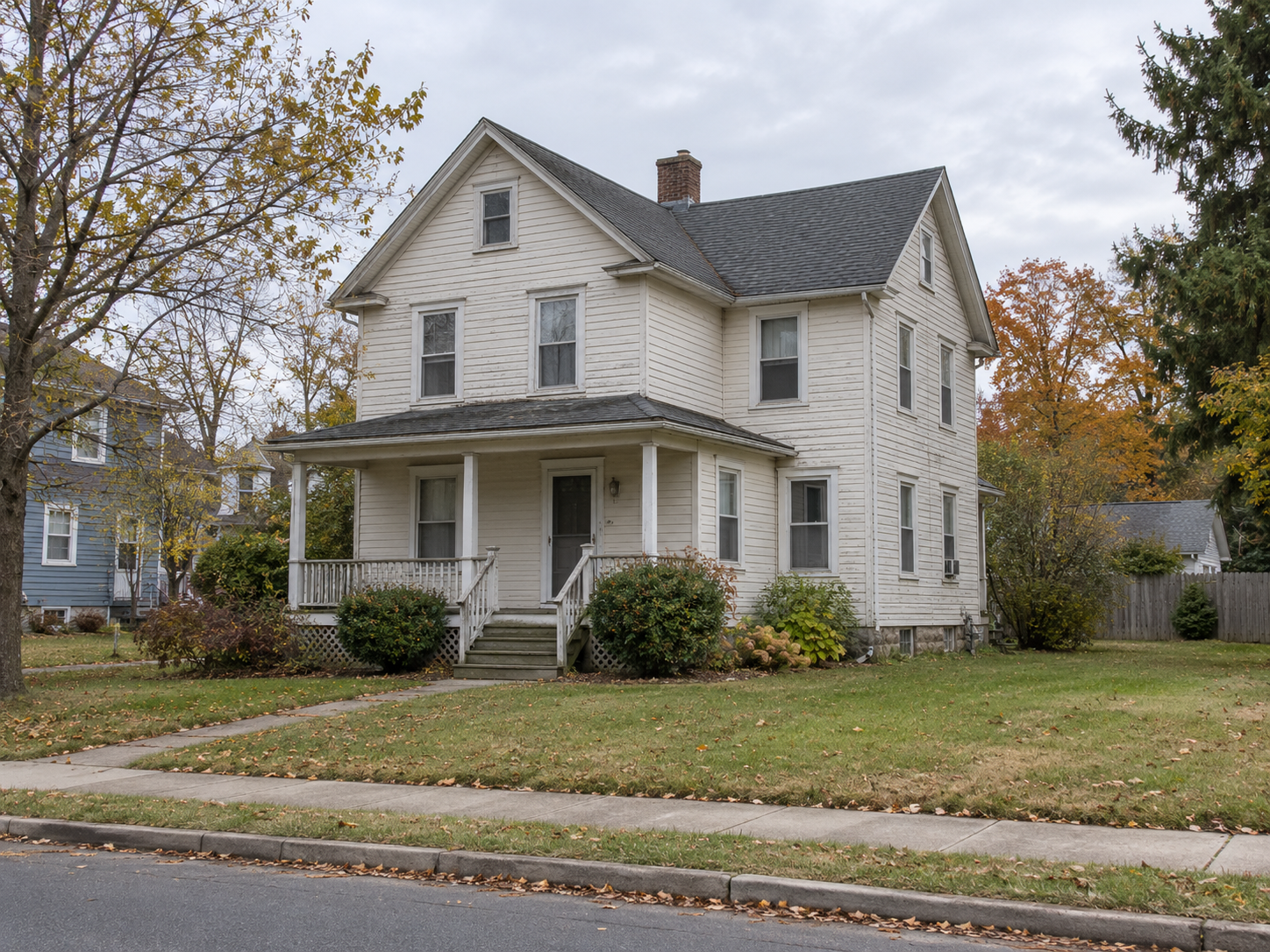 Older Northeast home with mature trees and weathered siding, viewed across the front yard