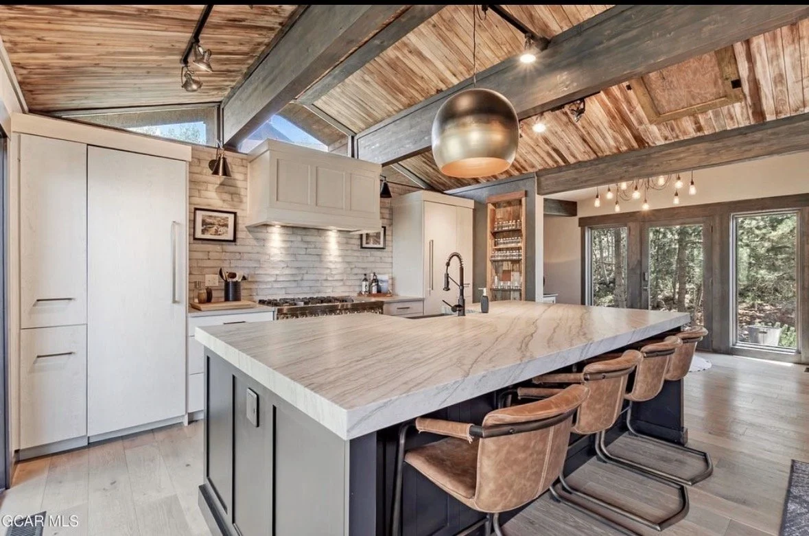 The kitchen with a long stone island under reclaimed-wood ceilings