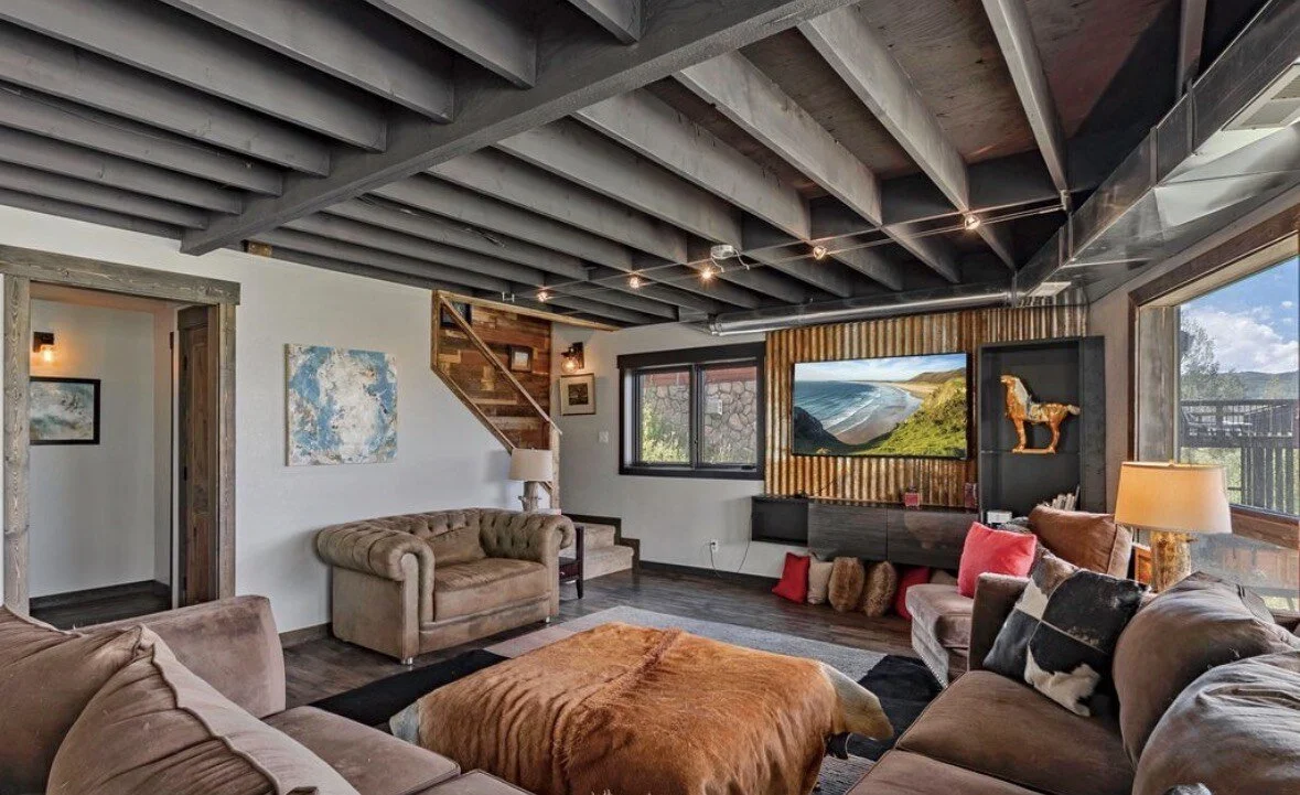 The lower-level lounge with a deep sectional, a cowhide ottoman and a big TV