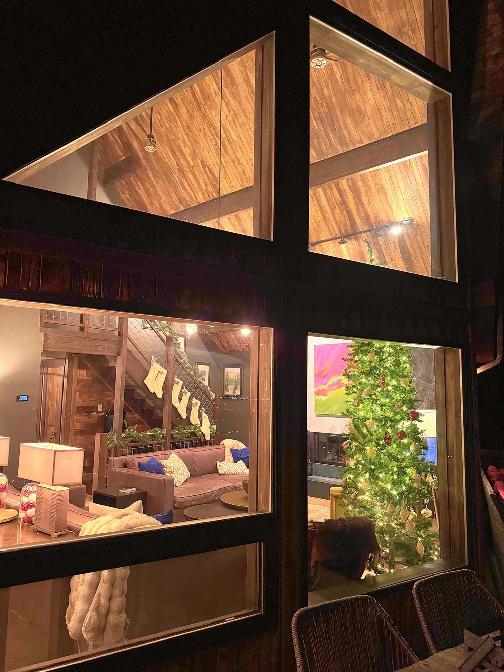 Looking in through the lodge's windows at night to the lit tree and stockings hung on the stairs
