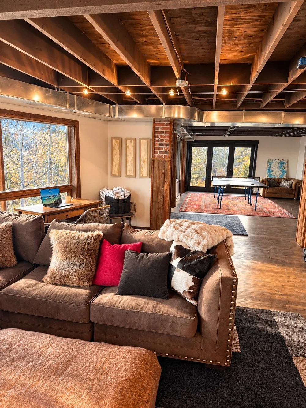 The lower-level lounge with a deep sectional, the desk by the window, and the ping pong table beyond