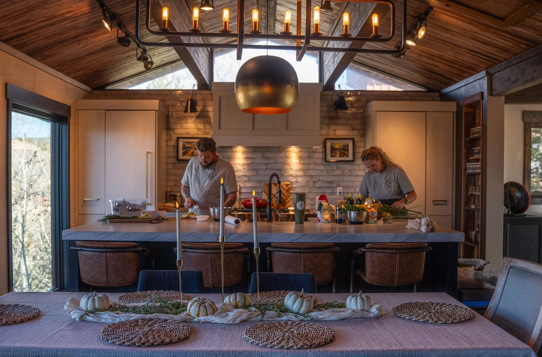 Two chefs cooking at the kitchen island while a long table is set for dinner