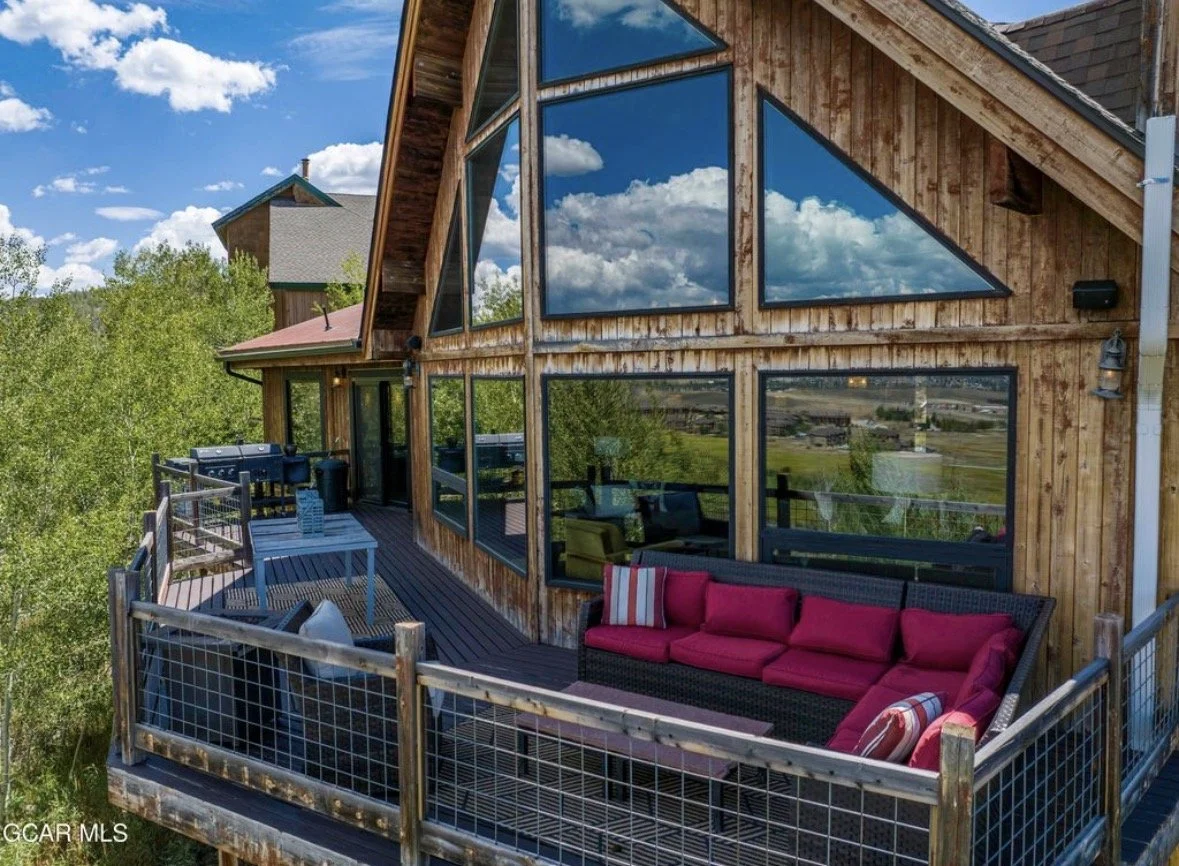 The deck sofas beneath tall gable windows reflecting the clouds