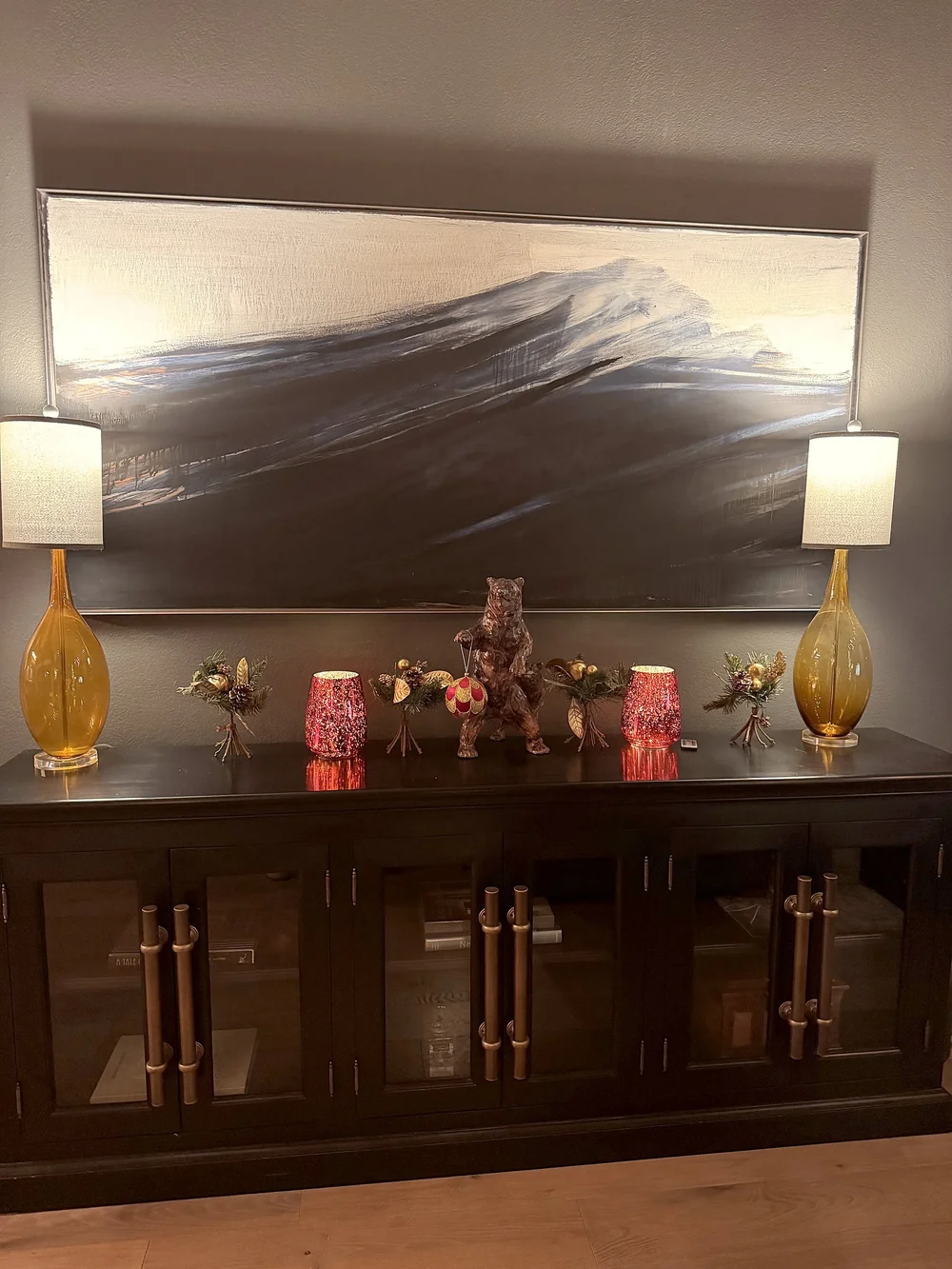 A sideboard with holiday decorations beneath a large mountain painting