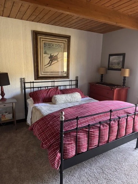 A queen bedroom with an iron bed, red plaid bedding and a vintage Black Dog ski poster