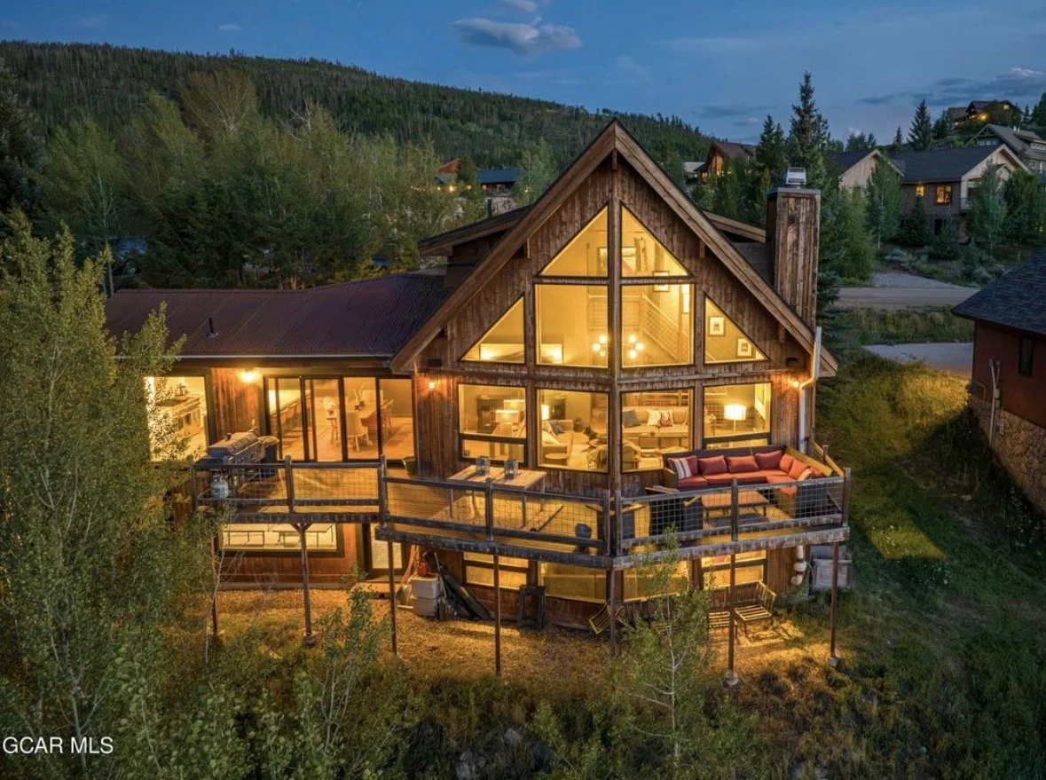Honeysuckle Lodge at dusk, its two-story gable windows glowing above the deck and aspens