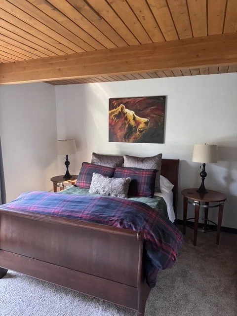 A queen bedroom with a sleigh bed, plaid bedding and a painting of a bear