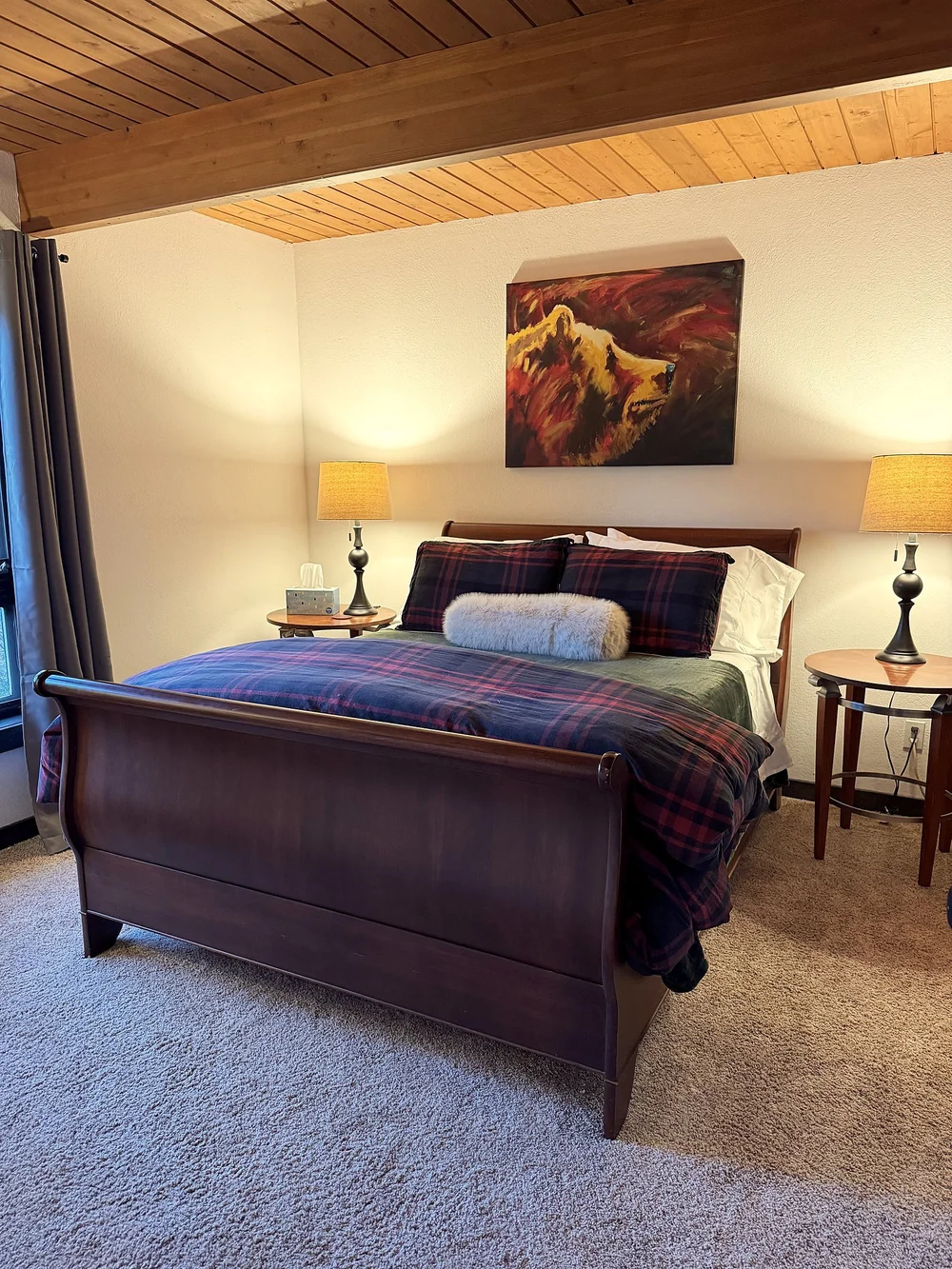 A queen bedroom with a sleigh bed, plaid bedding, bedside lamps and a painting of a bear