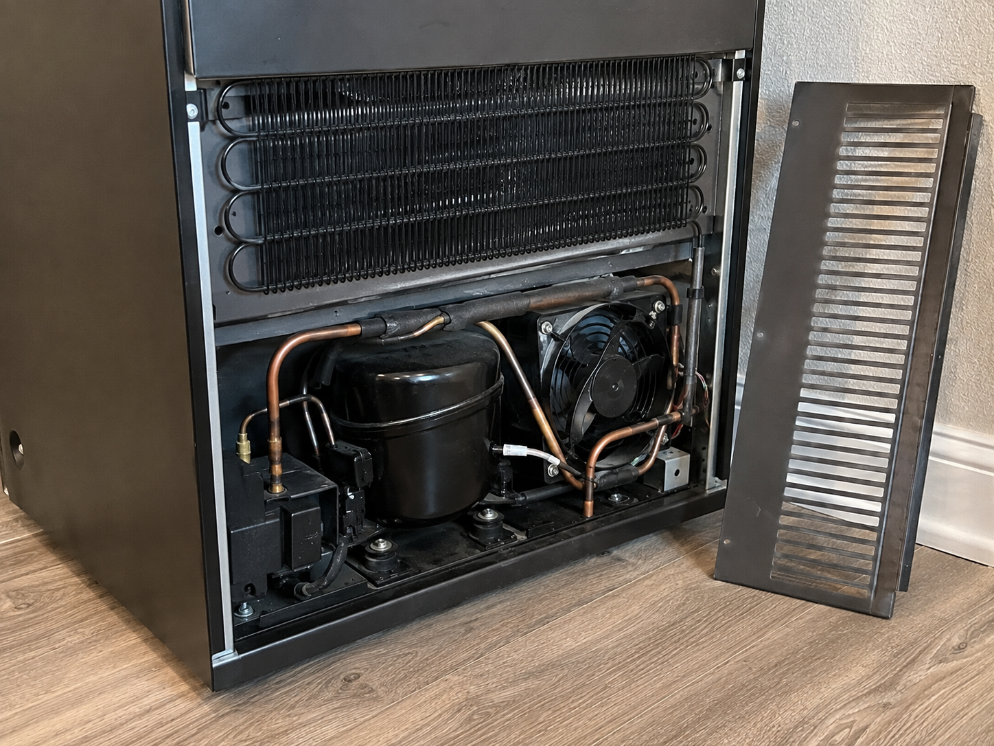 Under-counter wine and beverage cooler with its front grille removed, the compressor side of a cooler that a cold Post Falls room can quiet