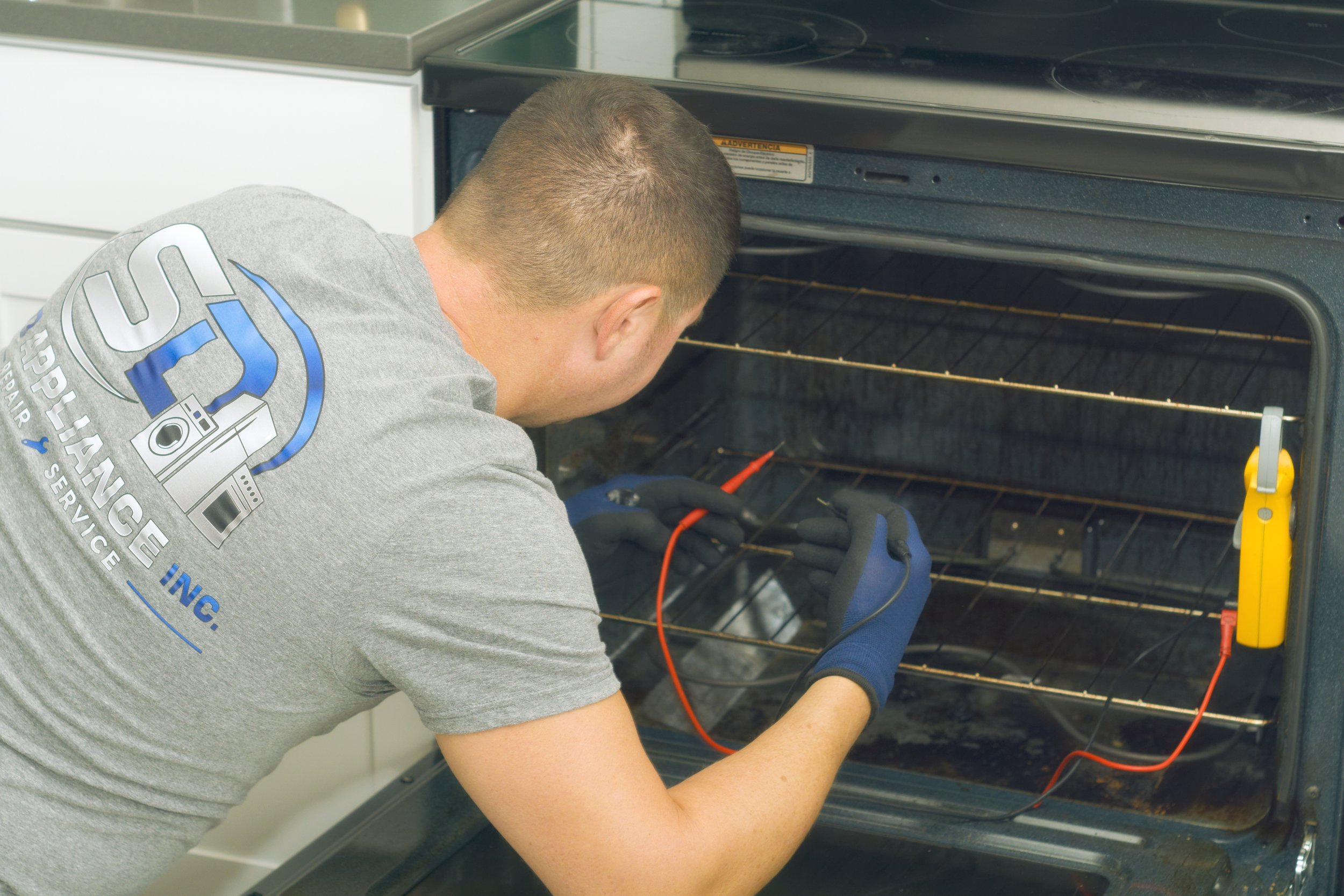 Tech in SD shirt inside an oven with meter probes during a Spokane oven repair by SD Appliance