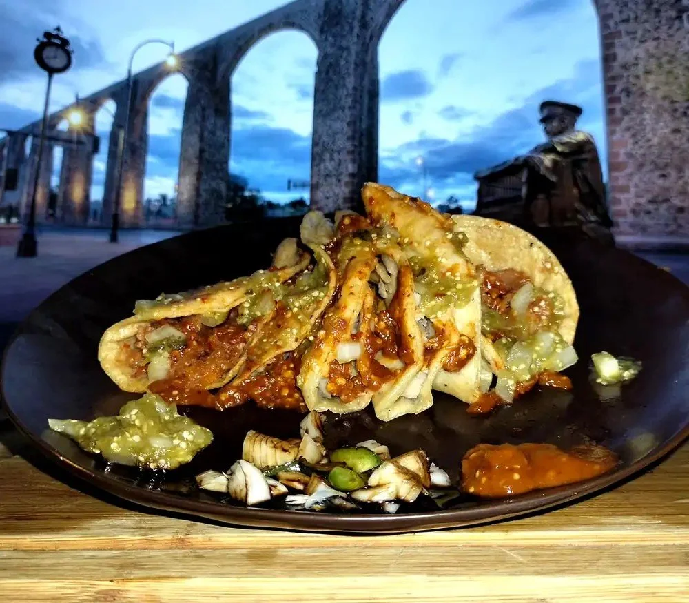Tacos de canasta Tacomible con salsa verde y roja frente a los Arcos de Querétaro