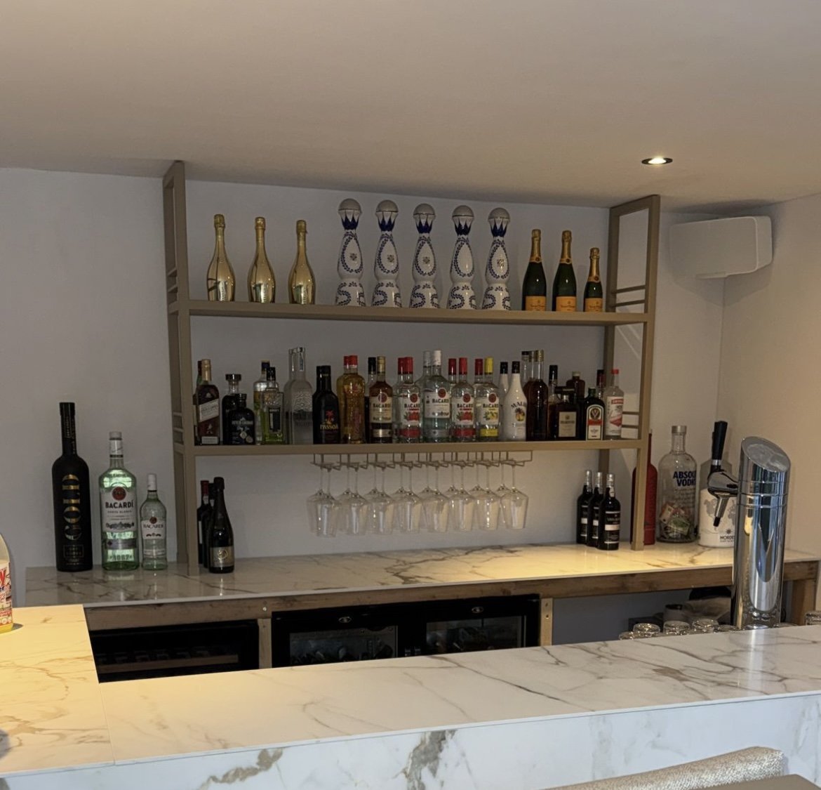 Achterwand van een bar met stalen flesschappen boven een stenen werkblad