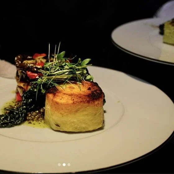 A golden fondant potato main course plated with charred vegetables and herbs