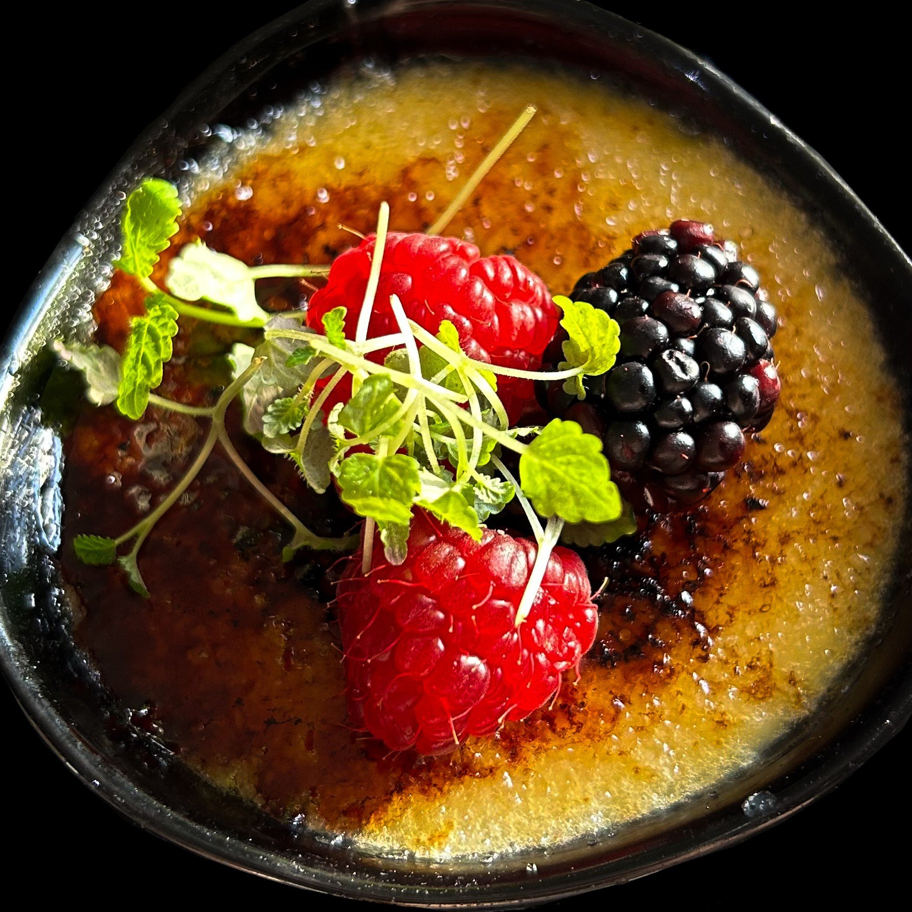 A crème brûlée dessert topped with fresh raspberries and blackberries