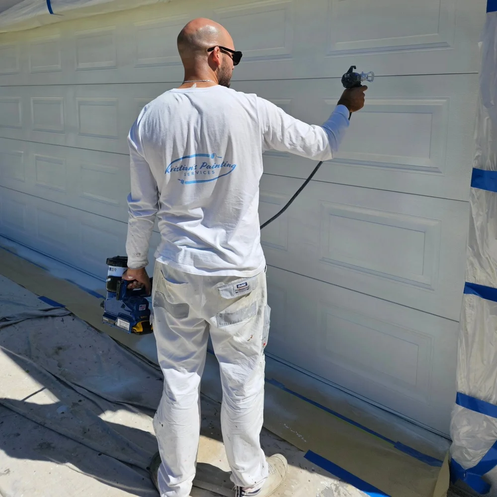 Kristian spray painting a residential garage door in Kristian’s Painting workwear