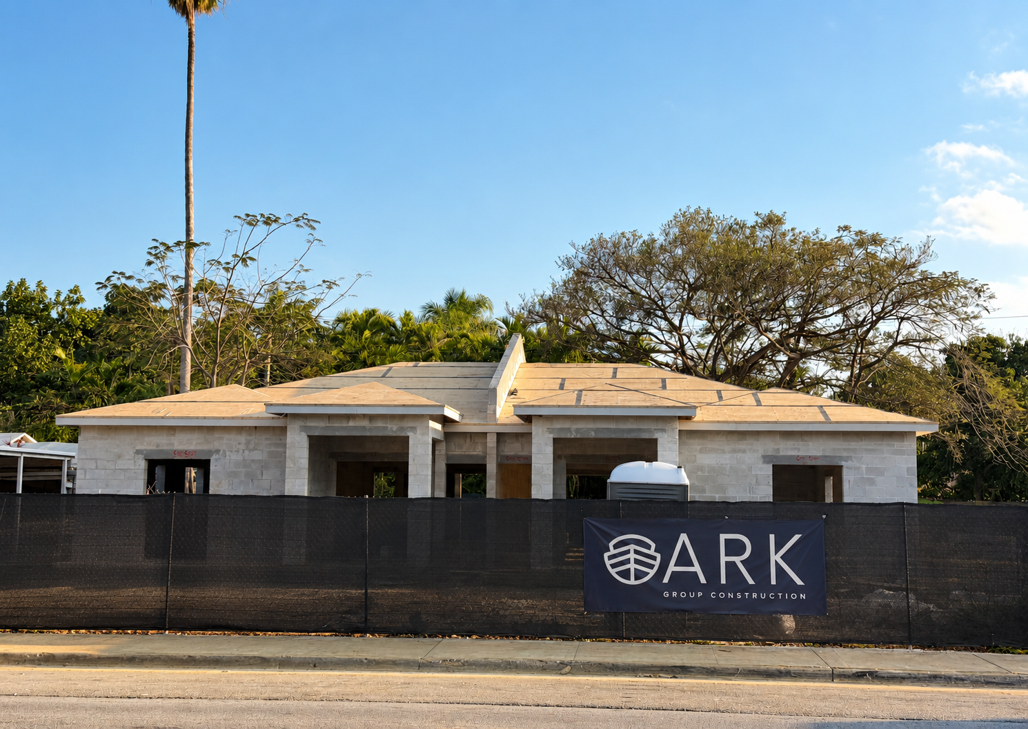 New-construction duplex under way on an infill lot, block walls up and roof sheathing on, with ARK Group Construction site signage