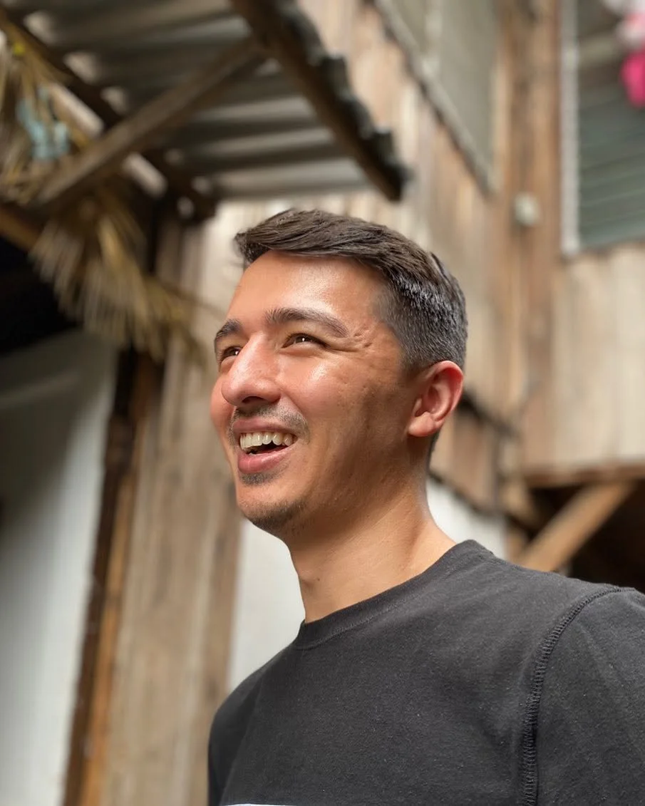 Tyler smiling beside a wooden building during his travels.