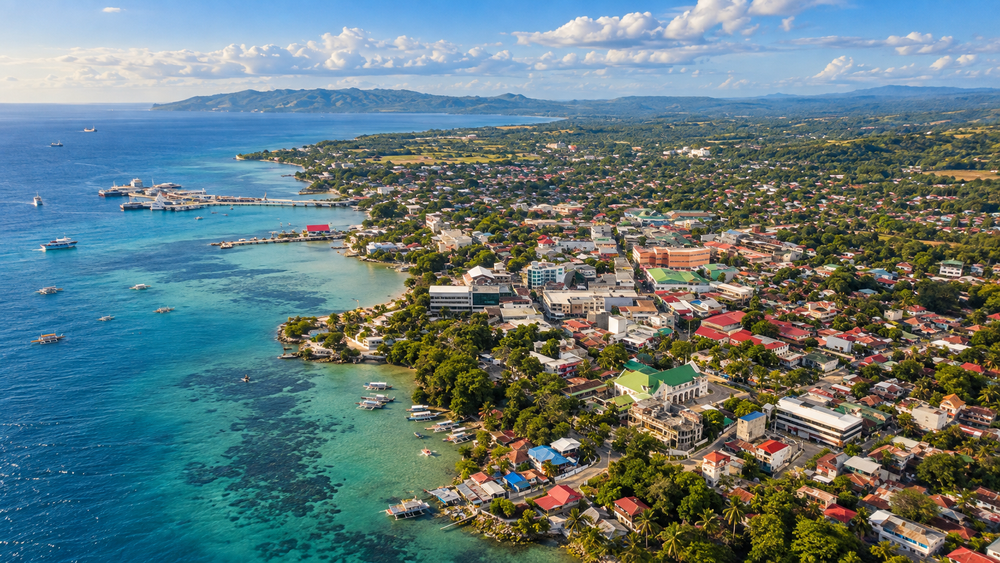 Bohol-inspired aerial view of blue coastal water, a town, and green countryside