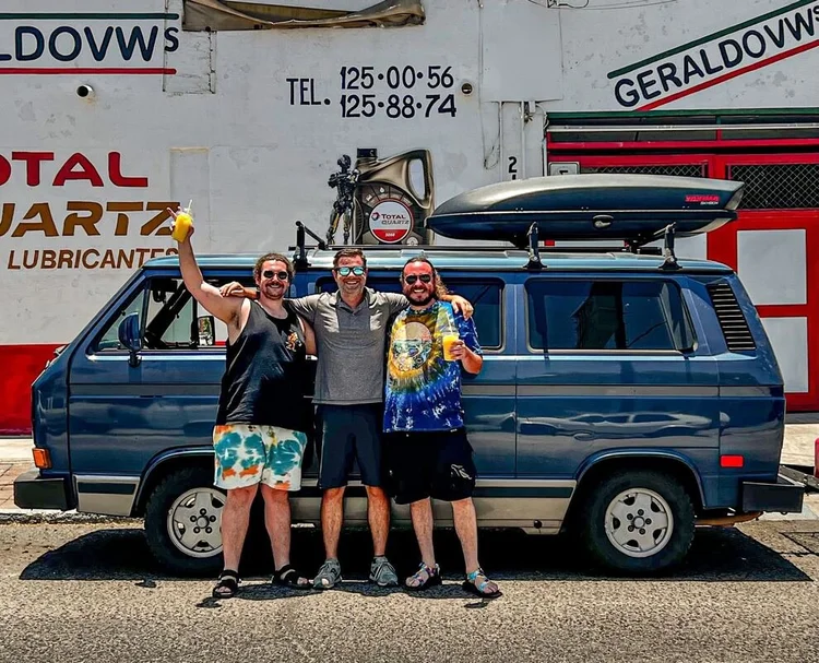 Three people beside a blue Volkswagen camper outside a workshop