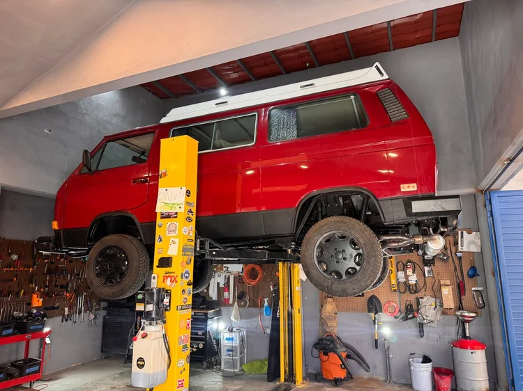 Red Volkswagen Vanagon with black wheels on a workshop lift