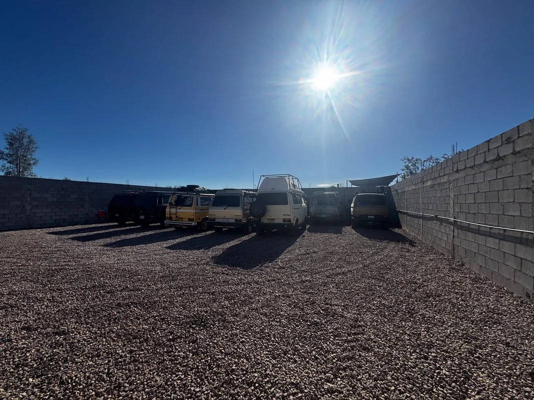 Camper vans parked on gravel within the walled vehicle storage yard in La Paz