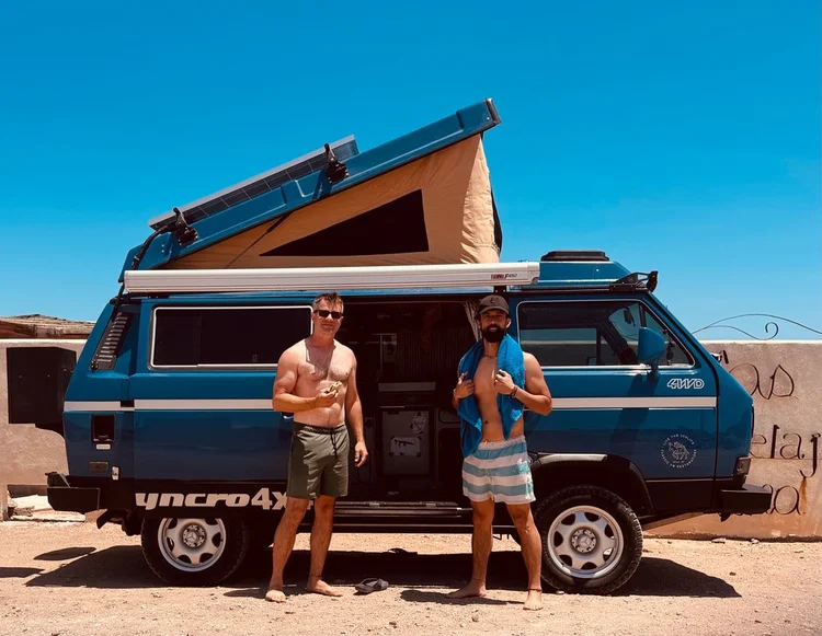 Two people beside a blue Volkswagen camper with its pop-top raised