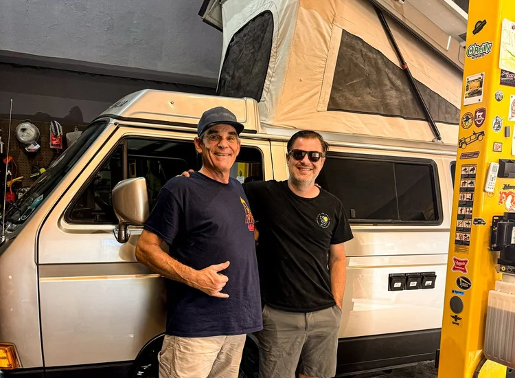 Two people beside a cream Volkswagen Westfalia inside the workshop