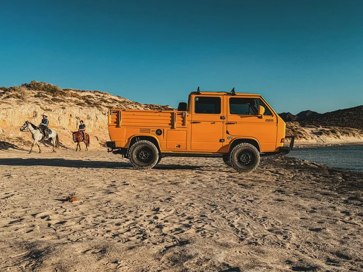 Orange Volkswagen double-cab pickup parked on a beach