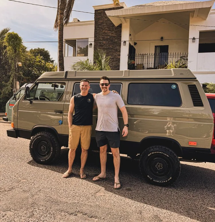 Two people beside a gray Volkswagen camper van