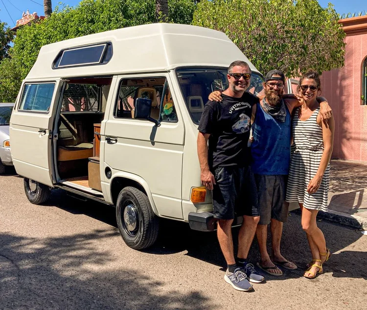 Three people beside a white high-roof Volkswagen camper